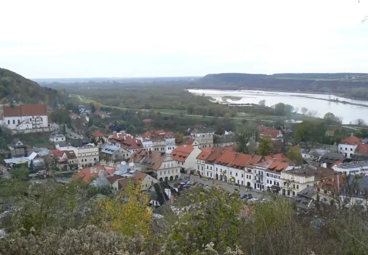 Widok na Kazimierz Dolny z rzeką Wisłą w tle. Planujesz podróż? Sprawdź, jak dojechać do Kazimierza Dolnego pociągiem.