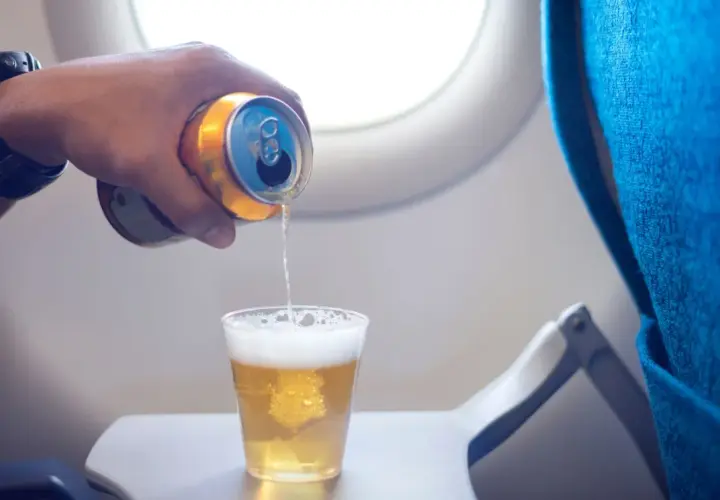 Ręka z puszką piwa nalewa napój do szklanki na stoliku w samolocie. Czy można przewozić alkohol samolotem?
