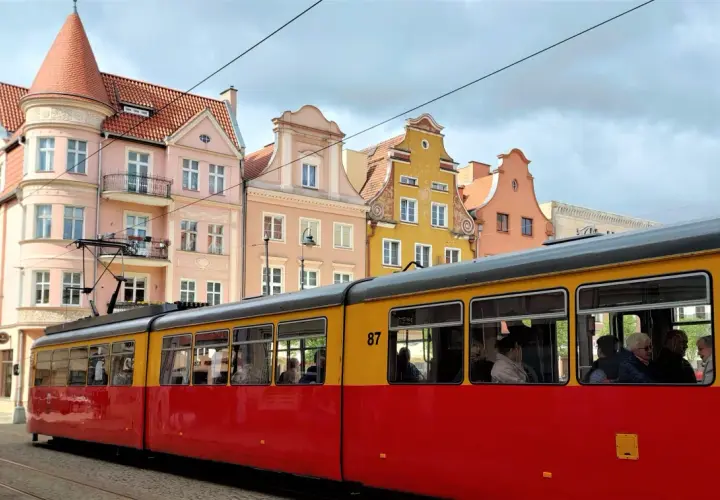 Czerwono-żółty tramwaj z numerem 87 jedzie ulicą Grudziądza. W tle kolorowe kamienice.