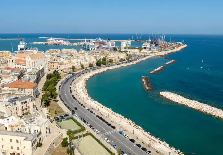 Widok na port w Bari, gdzie statki i dźwigi tworzą tło dla miejskiej komunikacji.
