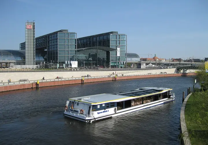 Statek wycieczkowy płynie wzdłuż Sprewy obok nowoczesnych budynków Berlin Hauptbahnhof, gdzie znajdują się perony.
