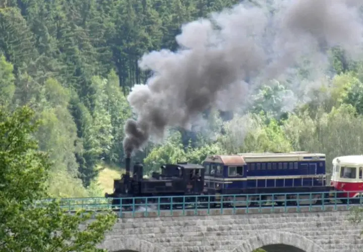Parowóz z wagonami na kamiennym wiadukcie. Kolej izerska z biletami zaprasza na malowniczą podróż przez las.