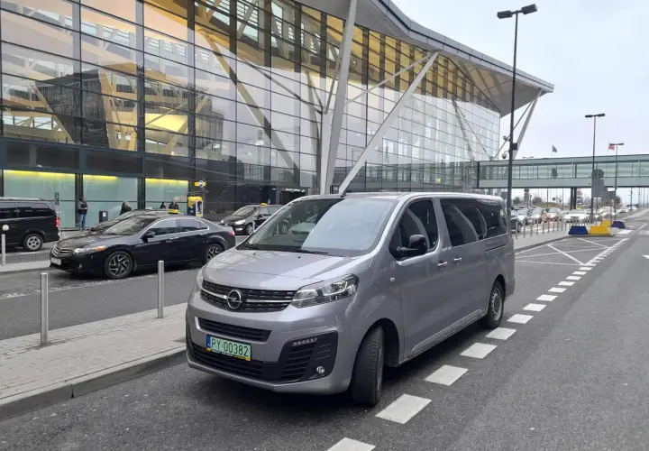 Srebrny bus czeka na pasażerów przed nowoczesnym terminalem lotniska. Może to być transport z Koszalina do Gdańska na lotnisko.