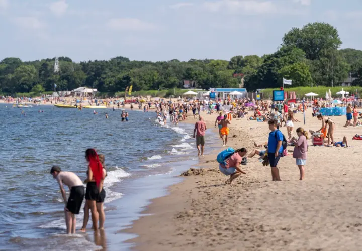 Ludzie cieszą się słońcem i morzem na plaży. W tle widać las. Idealne miejsce na podróż pociągiem nad morze z Poznania.