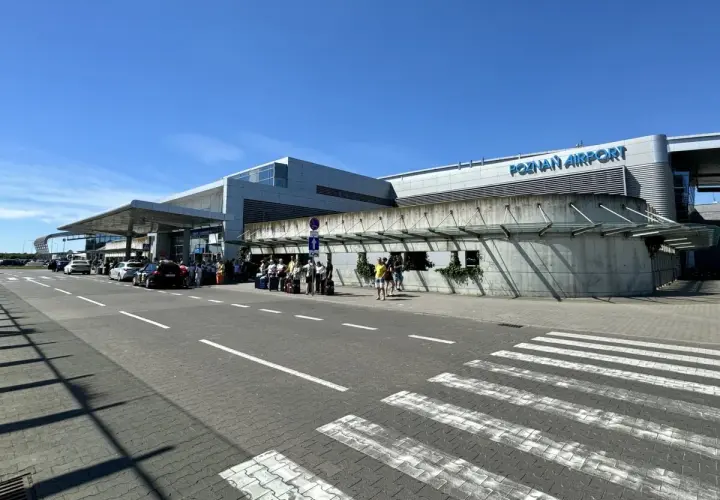Lotnisko Poznań Airport, z ludźmi i samochodami przed budynkiem. Tu znajdziesz informacje, jak dojechać z dworca PKP na lotnisko w Poznaniu.