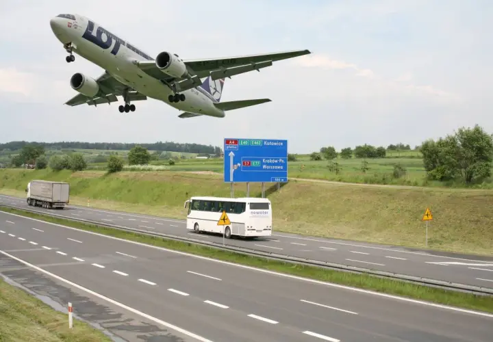 Samolot LOT leci nisko nad autostradą A4 w kierunku Katowic. Obok jedzie autobus, a w oddali widać drogę do Krakowa i Warszawy.