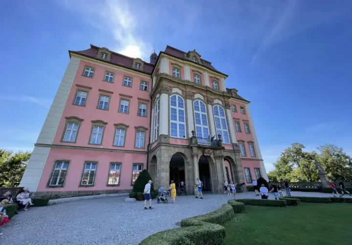 Zamek Książ, łatwy dojazd PKP, zachwyca różową fasadą i barokową architekturą. Turyści spacerują po brukowanym dziedzińcu.