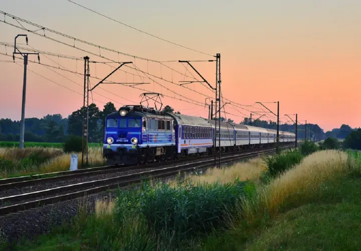 Niebieski pociąg PKP EP07-389 z wagonami mija pole o zachodzie słońca, jadąc w stronę Kołobrzegu.