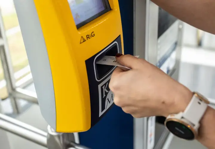 Ręka z zegarkiem wkłada bilet godzinny Kraków do żółtego automatu.