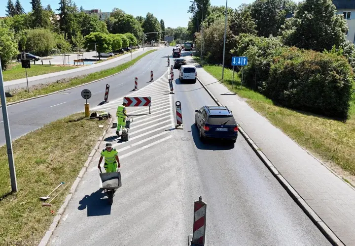 Prace drogowe na linii 101 Szczecin. Robotnicy w kamizelkach odblaskowych przygotowują nawierzchnię, jeden z nich pcha taczkę z materiałem.
