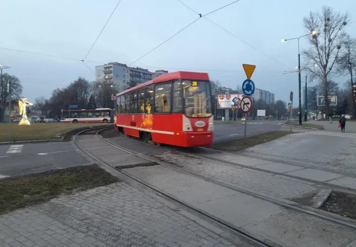 Czerwony ztm 26 tramwaj przejeżdża przez skrzyżowanie. W tle widać autobus i budynki.
