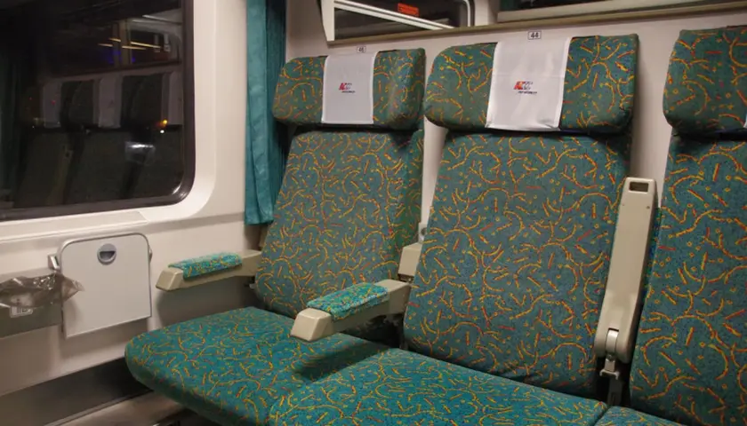Wnętrze wagonu PKP Intercity. Widok na dwa rzędy siedzeń z charakterystycznym wzorem. Wybór miejsca ze schematu jest kluczowy dla komfortowej podróży.