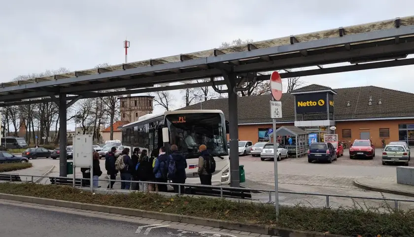 Ludzie czekają na autobus pod wiatą przystankową w Poznaniu Mielnie, obok sklepu Netto.