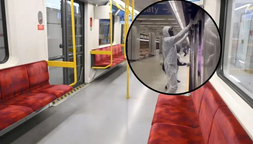 Wnętrze pustego wagonu metra M2, gdzie pracownicy w kombinezonach dezynfekują drzwi.