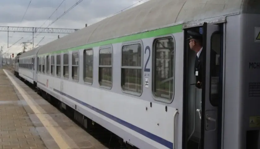 Konduktor w czapce stoi w otwartych drzwiach pociągu z zieloną górą, gotowy do odjazdu ze Szczecina.