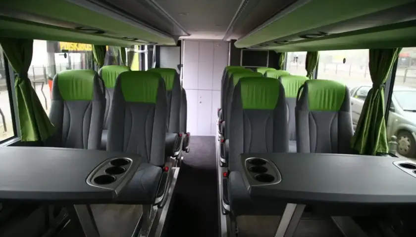 Wygodne, zielono-szare fotele w autobusie FlixBus, z rozkładanymi stolikami i uchwytami na kubki.