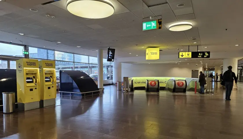 Żółte automaty biletowe Arlanda Express i schody ruchome prowadzące do pociągu.