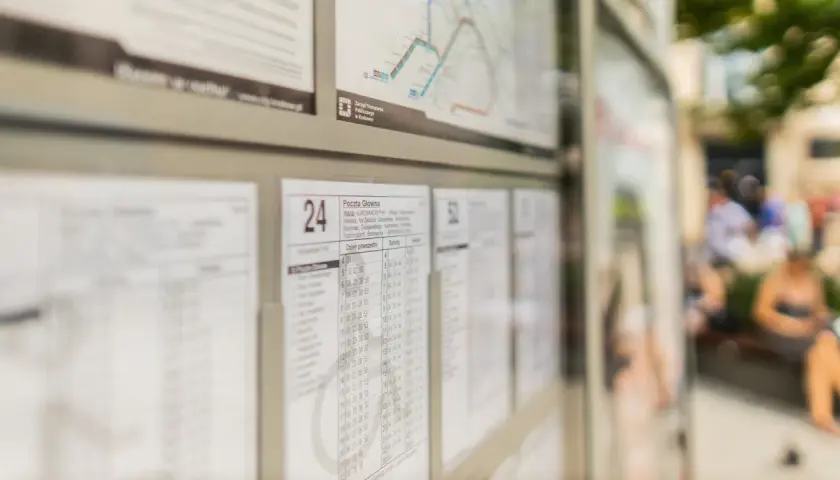 Rozkład jazdy autobusów Kraków. Widoczne tablice z godzinami odjazdów, mapka linii i ludzie czekający na przystanku.