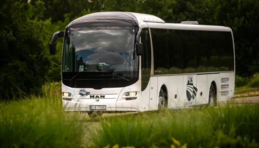 Biały autokar PKS z Jarosławia jedzie przez zielony, bujny krajobraz.