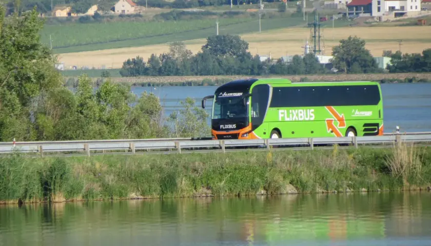 Zielony autobus Flixbus jedzie wzdłuż jeziora. Szukaj flixbus promocje na podróż!