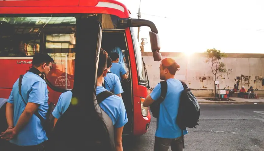 Grupa młodych ludzi z gitarą wsiada do czerwonego autobusu GTV. Słońce zachodzi, tworząc ciepłą atmosferę.