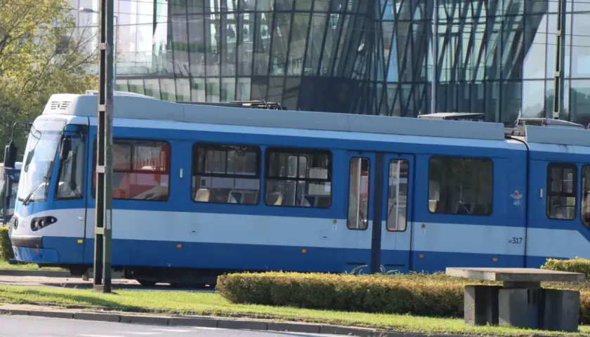 Niebieski tramwaj MPK Kraków stoi na tle nowoczesnego budynku. Sprawdź aktualny mpk kraków bilety cennik przed podróżą.