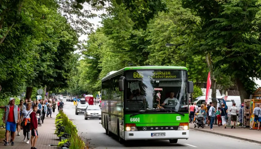 Zielony autobus linii 666 jedzie w kierunku Karwii i Jastrzębiej Góry. Na poboczu spacerują ludzie, ciesząc się letnim dniem.