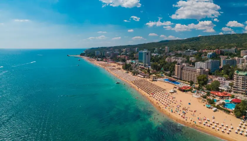 Słoneczna plaża w Złote Piaski, z turkusowym morzem i hotelami w tle. Idealne miejsce na wakacje, niedaleko lotniska.