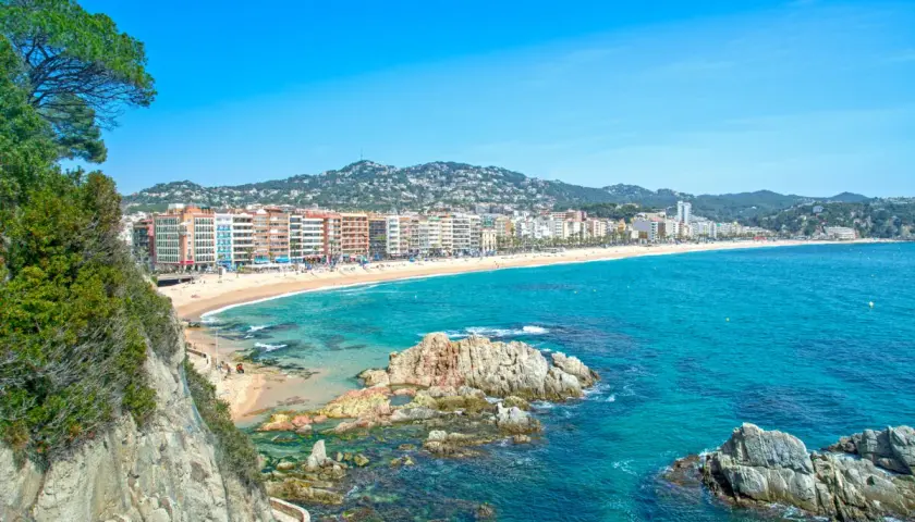 Widok na plażę w Lloret de Mar z klifów. W oddali widać zabudowania i wzgórza. Idealne miejsce na wakacje, niedaleko od lotniska.