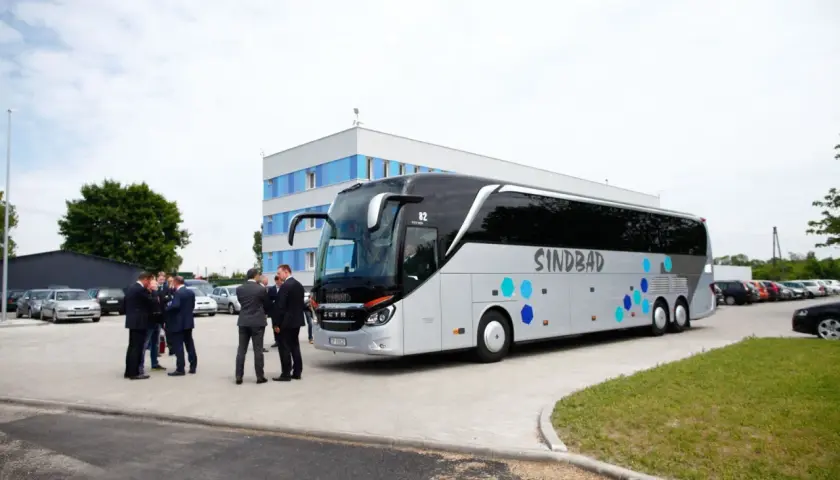 Grupa mężczyzn w garniturach rozmawia przy autokarze Sindbad. Sprawdzają ceny biletów przed podróżą.
