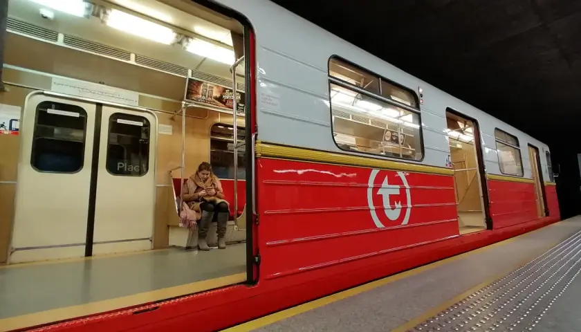 Kobieta czeka na swiateczne metro. Czerwony wagon z białym logo.
