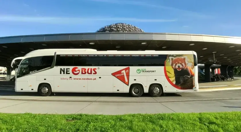 Biały autokar Neobus z pandą małą na boku stoi pod nowoczesnym zadaszeniem. Sprawdź neobus ceny biletów na www.neobus.pl.