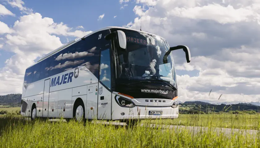 Autobus Majer na trasie Kraków - Mszana Dolna jedzie przez zielone pola pod błękitnym niebem.