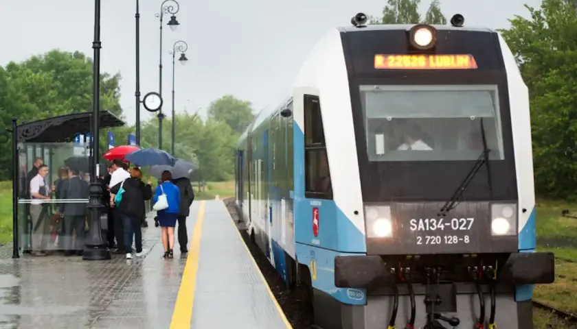 Pasażerowie z parasolami czekają na peronie na pociąg Kolei Lubelskich.