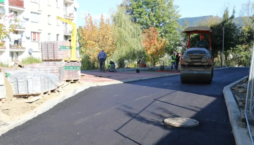 Prace drogowe na osiedlu Zygmunta Augusta w Limanowej. Walec drogowy ubija asfalt, a pracownicy układają kostkę.