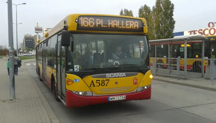 Żółty autobus linii 166 w Warszawie, z numerem bocznym A587, zbliża się do przystanku obok centrum handlowego Tesco.