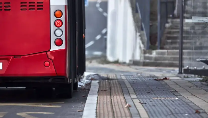 Czerwony autobus 74 stoi na przystanku. Widać jego tylne światła i część karoserii.