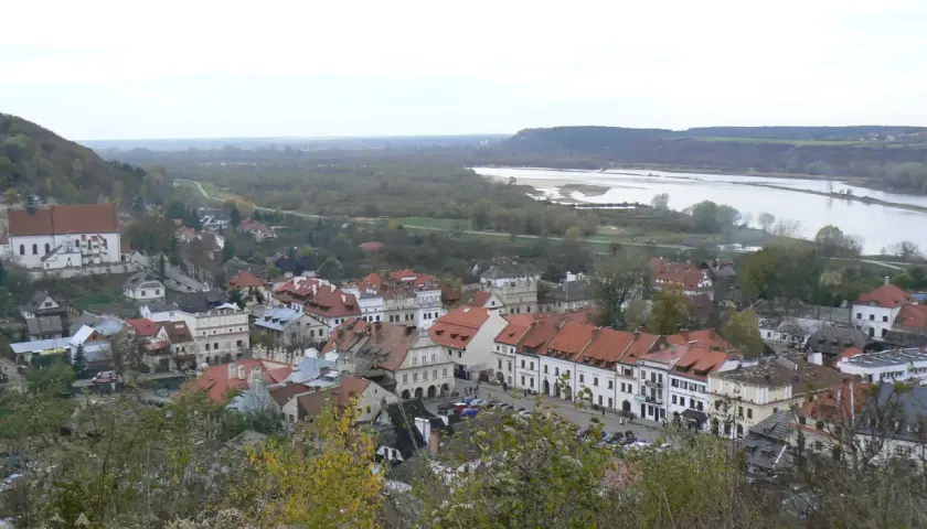 Widok na Kazimierz Dolny z rzeką Wisłą w tle. Planujesz podróż? Sprawdź, jak dojechać do Kazimierza Dolnego pociągiem.