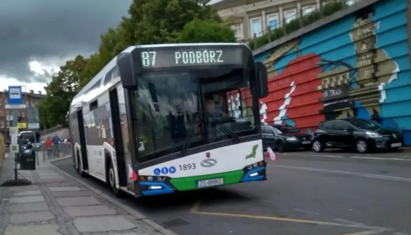 Autobus linii 87 w Szczecinie z napisem "Podwórze" na wyświetlaczu, zbliża się do przystanku.