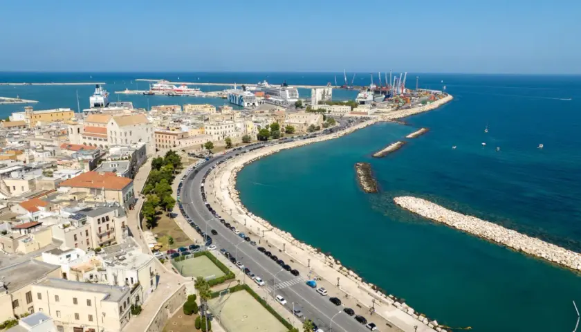 Widok na port w Bari, gdzie statki i dźwigi tworzą tło dla miejskiej komunikacji.