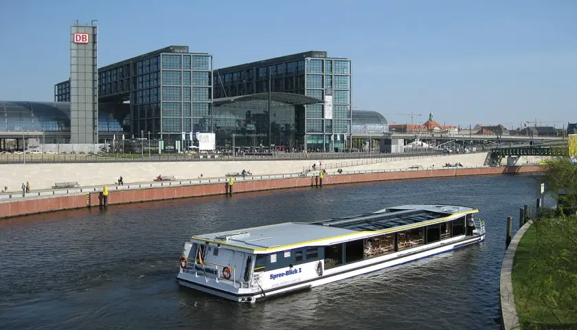 Statek wycieczkowy płynie wzdłuż Sprewy obok nowoczesnych budynków Berlin Hauptbahnhof, gdzie znajdują się perony.