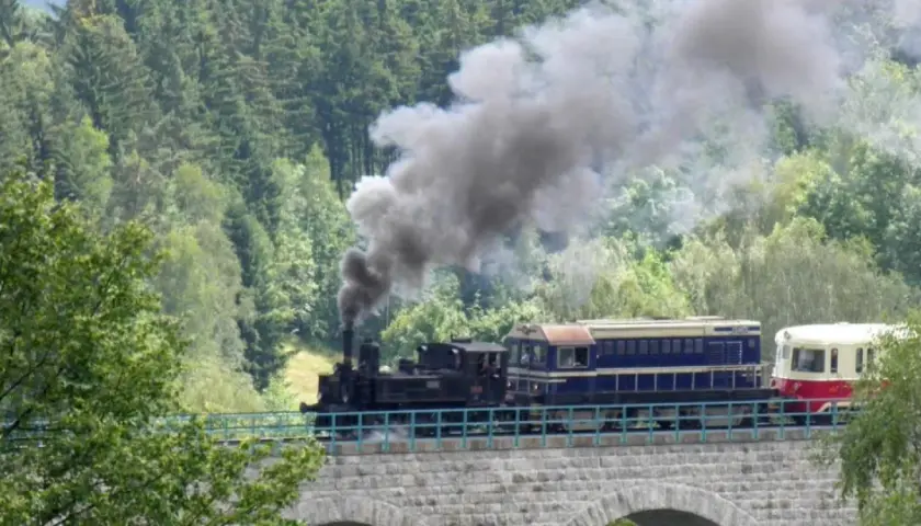 Parowóz z wagonami na kamiennym wiadukcie. Kolej izerska z biletami zaprasza na malowniczą podróż przez las.