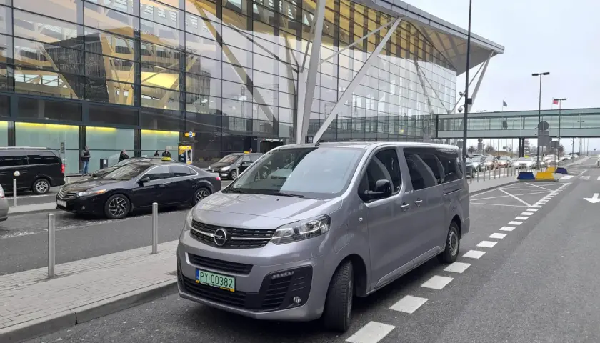 Srebrny bus czeka na pasażerów przed nowoczesnym terminalem lotniska. Może to być transport z Koszalina do Gdańska na lotnisko.
