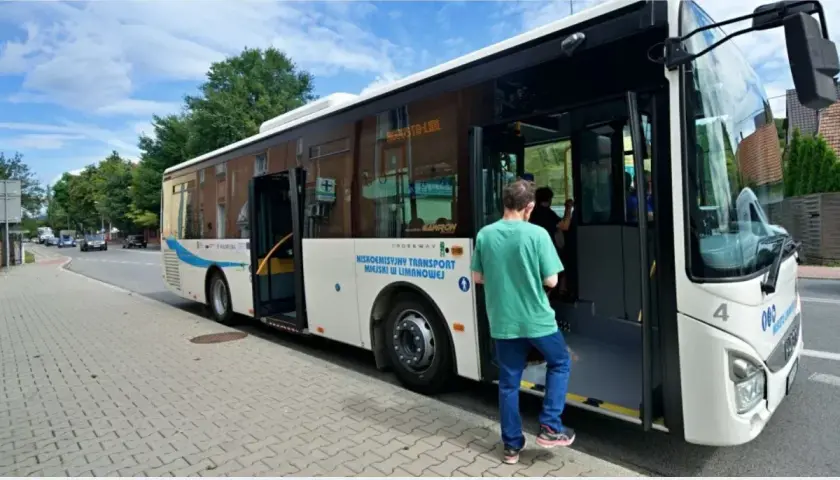 Biały autobus miejski z otwartymi drzwiami, wsiada pasażer.