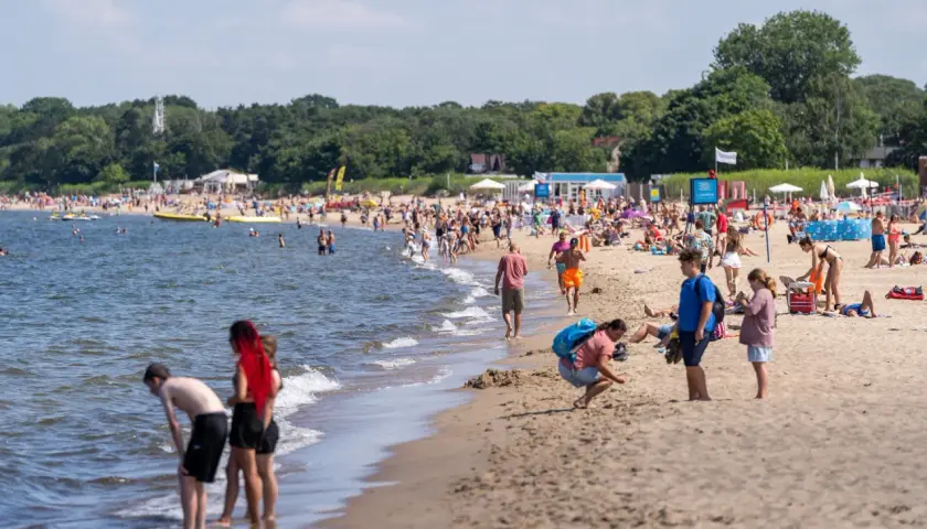 Ludzie cieszą się słońcem i morzem na plaży. W tle widać las. Idealne miejsce na podróż pociągiem nad morze z Poznania.