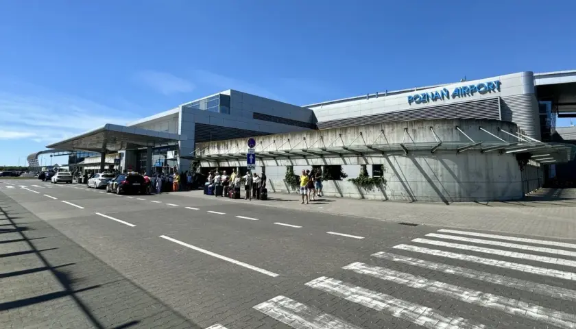 Lotnisko Poznań Airport, z ludźmi i samochodami przed budynkiem. Tu znajdziesz informacje, jak dojechać z dworca PKP na lotnisko w Poznaniu.