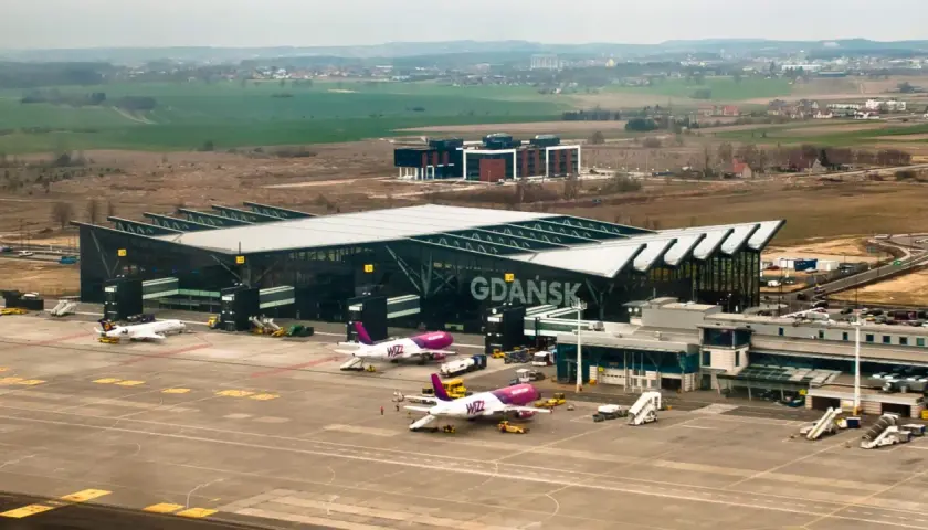 Samoloty Wizz Air i Lufthansa na płycie lotniska Gdańsk. W tle nowoczesny terminal i krajobraz.