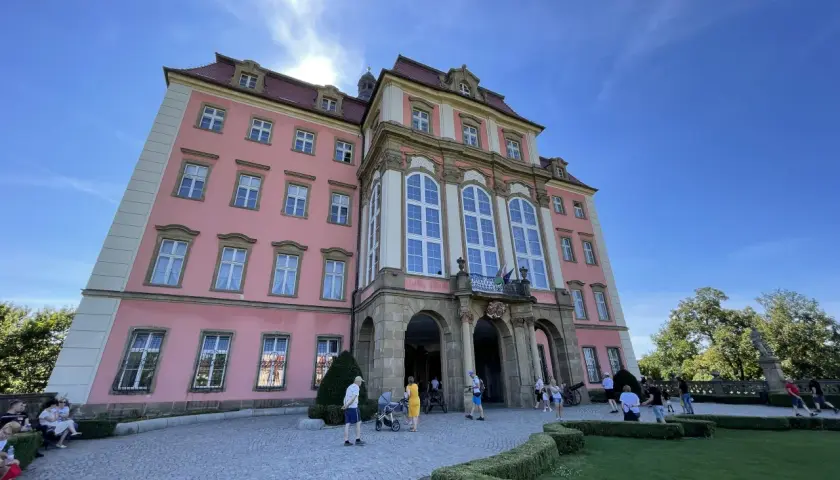Zamek Książ, łatwy dojazd PKP, zachwyca różową fasadą i barokową architekturą. Turyści spacerują po brukowanym dziedzińcu.