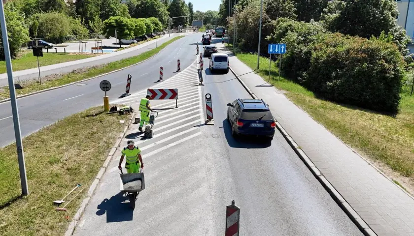 Prace drogowe na linii 101 Szczecin. Robotnicy w kamizelkach odblaskowych przygotowują nawierzchnię, jeden z nich pcha taczkę z materiałem.