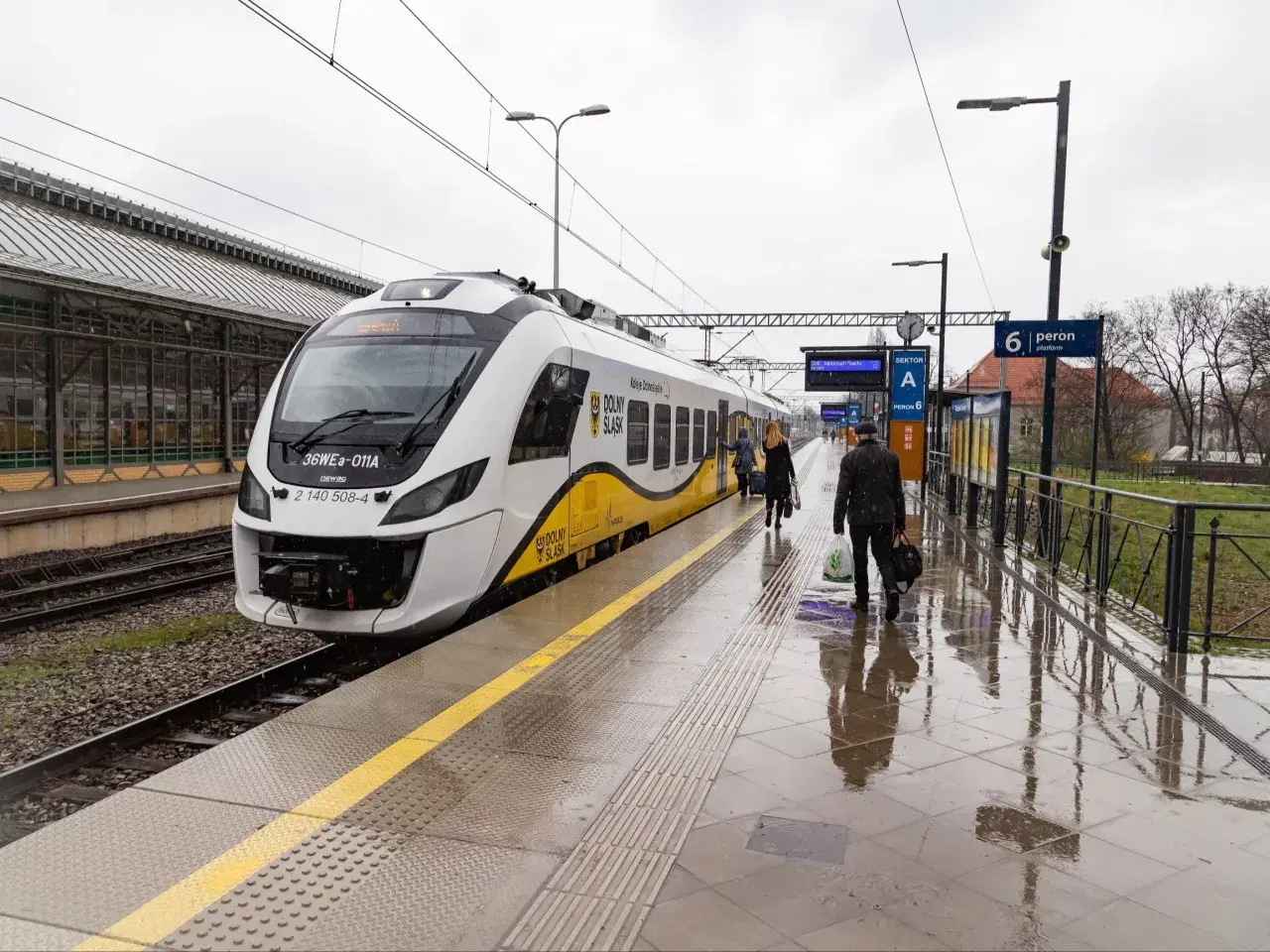 Pasażerowie wsiadają do pociągu, a obok stoi hulajnoga elektryczna.